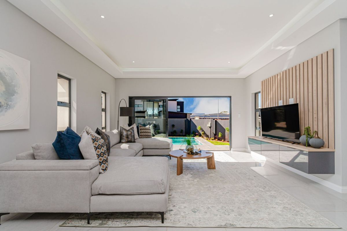 Modern living room featuring a timber slat feature wall, floating cabinetry, recessed ceiling lighting, and large sliding glass doors opening to the pool area.