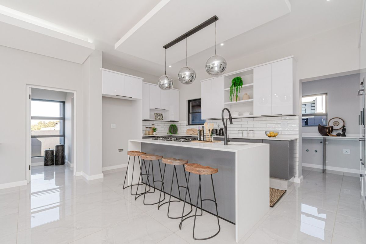Modern kitchen featuring a central island with gas hob, sleek white and grey cabinetry, subway tile backsplash, and contemporary pendant lighting.