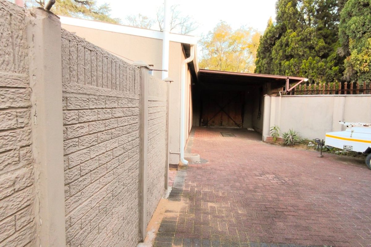 Rear exterior view showing a paved driveway, precast concrete boundary wall, and a covered carport area.