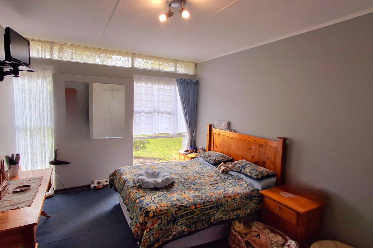 A functional bedroom featuring built-in cupboards, a large window providing natural light, and neutral wall finishes.