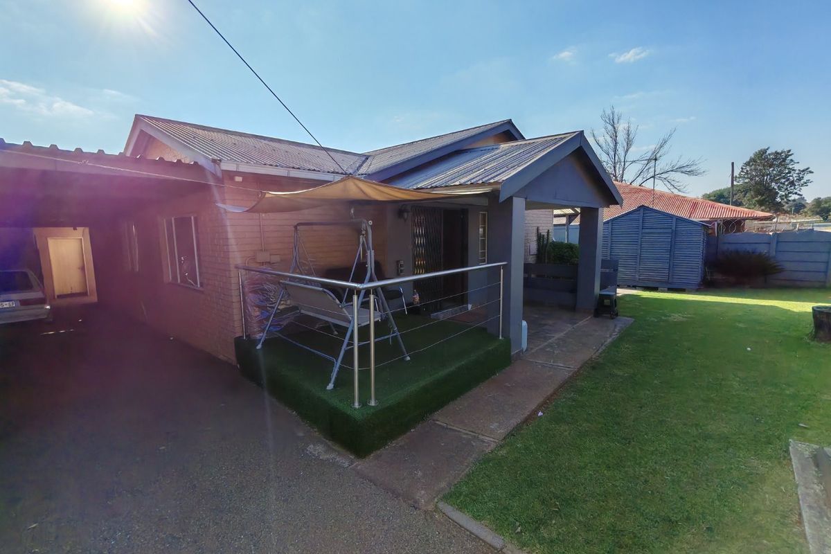 Rear view of the property featuring a covered patio with stainless steel balustrades, artificial grass, and an adjacent carport area.