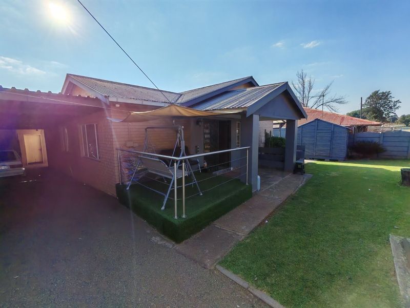 Rear view of the property featuring a covered patio with stainless steel balustrades, artificial grass, and an adjacent carport area.