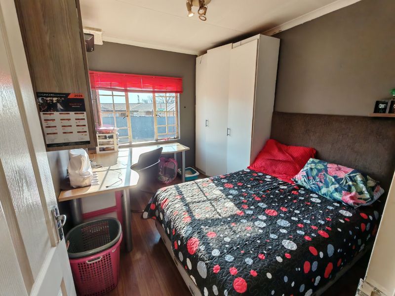 A functional bedroom featuring laminate flooring, a built-in wardrobe, and a window with security bars, offering a practical living space.