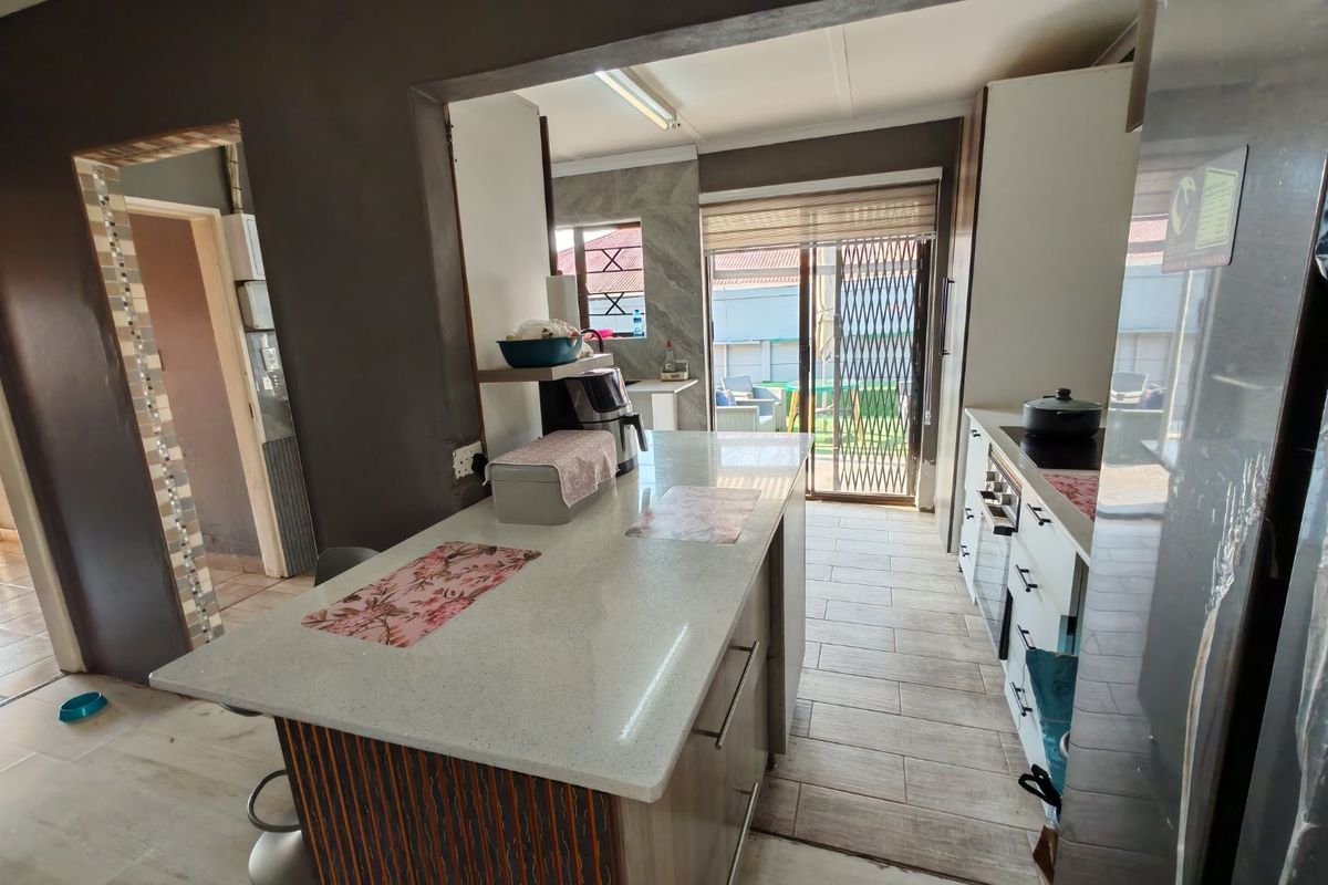 Modern kitchen featuring a central island with stone countertops, built-in cabinetry, integrated oven and hob, and direct access to the outdoor patio area.