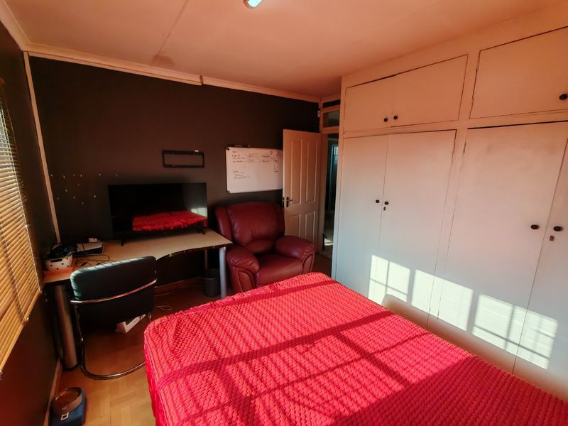 A bedroom featuring built-in cupboards, laminate flooring, and venetian blinds. The room requires cosmetic updates to improve its overall condition and appeal.