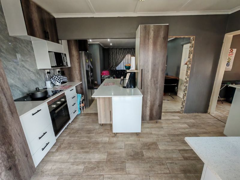 Modern kitchen featuring wood-look laminate cabinetry, stone countertops, a central island, and built-in appliances with durable tiled flooring.