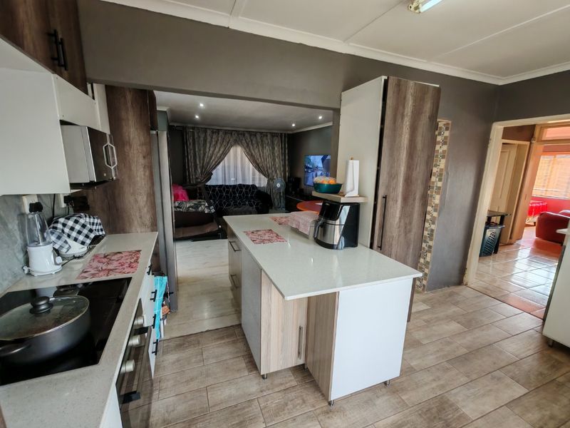 Open plan kitchen featuring a central island with stone countertops, modern cabinetry, and tiled flooring, seamlessly flowing into the adjacent living area.
