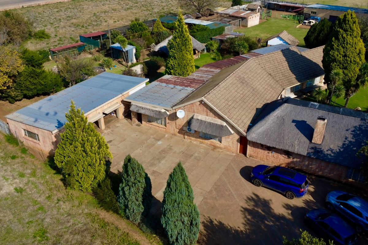 Aerial view of a farm property featuring a main residence with a combination of thatched and corrugated metal roofing, paved driveway, and surrounding outbuildings.