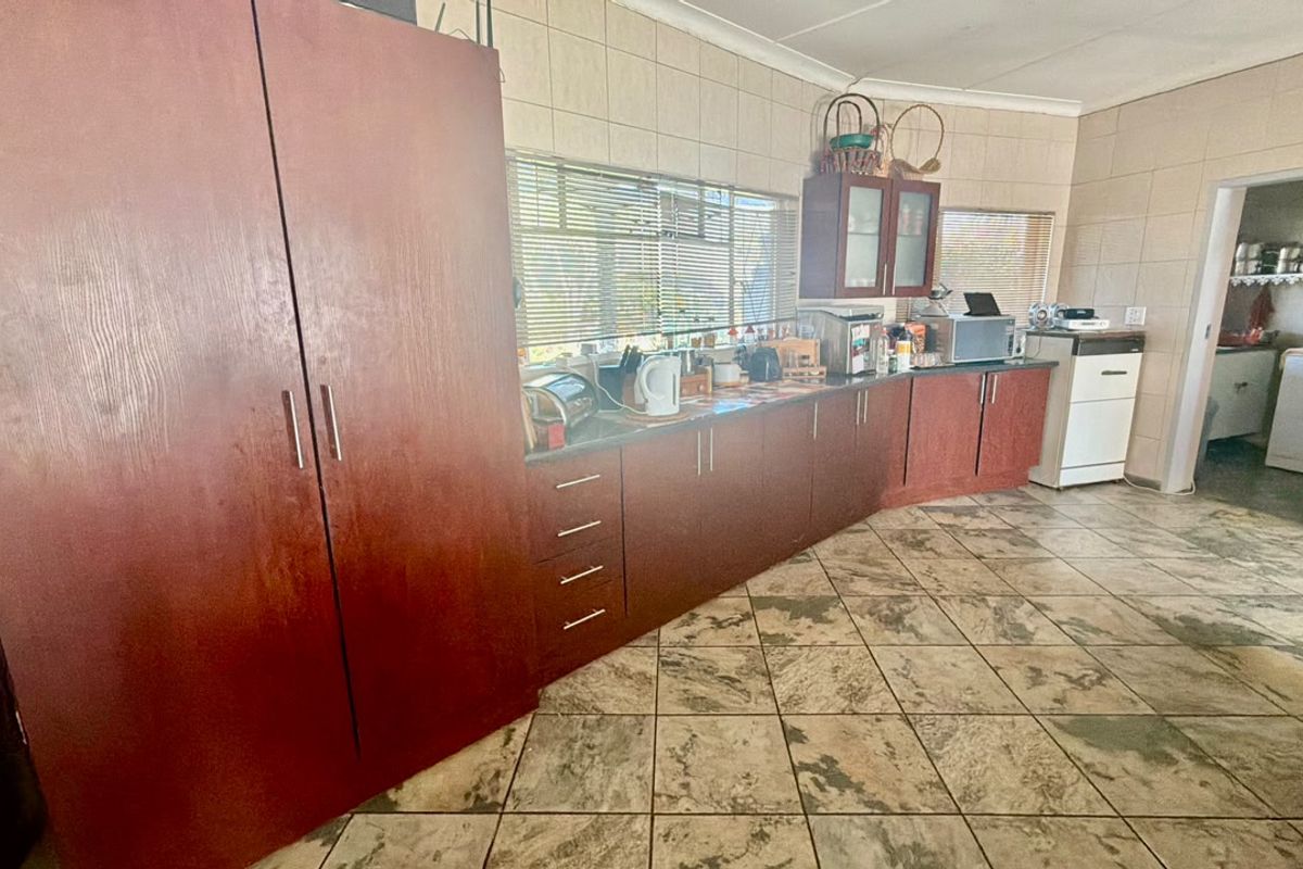 A functional kitchen featuring extensive built-in wooden cabinetry, tiled flooring, and a tiled backsplash, with an adjacent utility area visible.