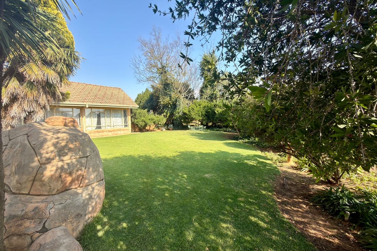 A spacious rear garden featuring a well-maintained lawn, mature landscaping, and a large decorative boulder, with a view of the rear building elevation.
