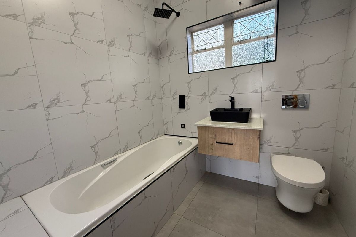 Modern bathroom featuring marble-effect wall tiles, a wall-mounted vanity with a vessel sink, a wall-hung toilet, and a built-in bathtub with a rain shower.