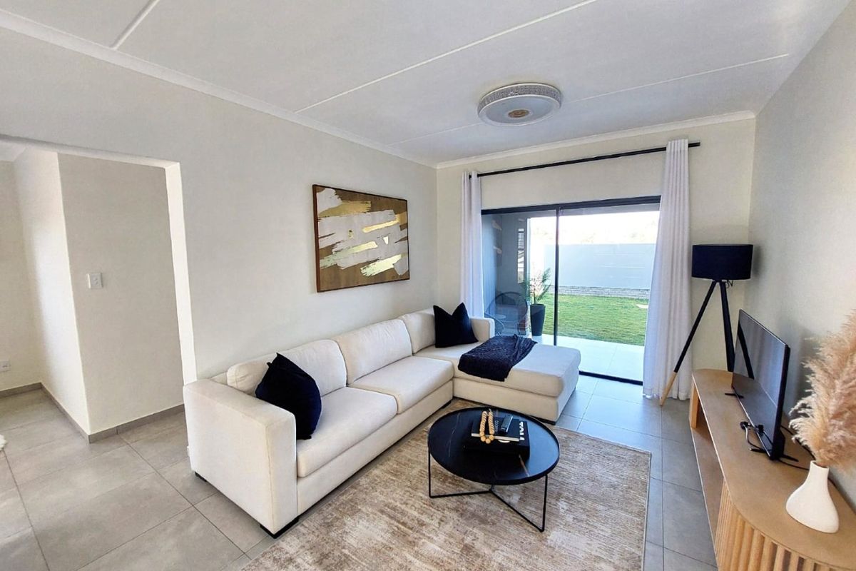 A bright and modern living room featuring neutral tiled flooring and a large sliding glass door providing direct access to the outdoor patio and garden.