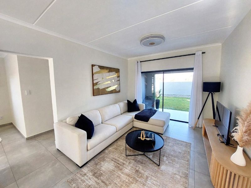 A bright and modern living room featuring neutral tiled flooring and a large sliding glass door providing direct access to the outdoor patio and garden.