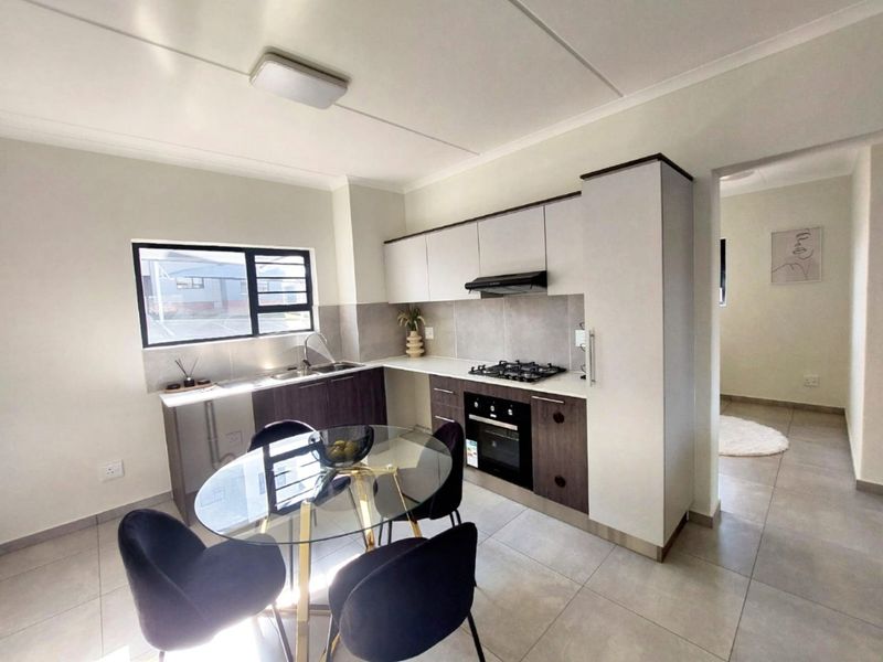 Modern open-plan kitchen featuring two-tone cabinetry, gas hob, electric oven, extractor fan, and tiled finishes, seamlessly integrated with the dining area.