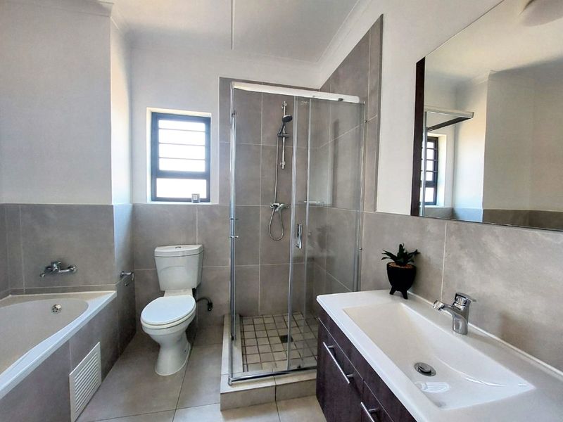 Modern bathroom featuring a glass-enclosed shower, built-in bathtub, vanity with basin, and neutral wall and floor tiling.