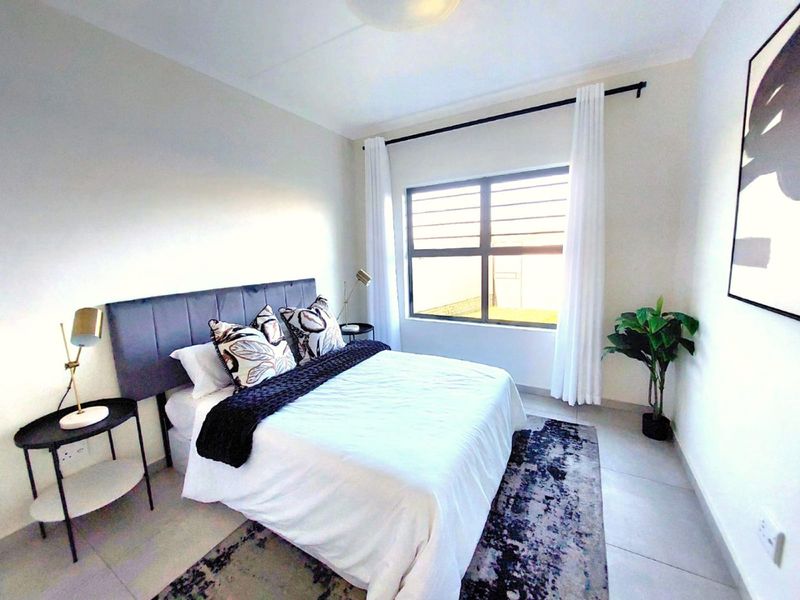 A well-maintained bedroom featuring neutral tiled flooring, a large window with curtain rod, and clean wall finishes.