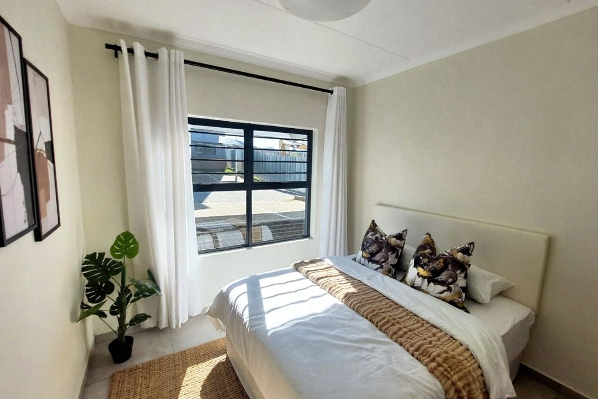 A well-lit bedroom featuring neutral wall tones, tiled flooring, and a large window with security bars, providing a clean and comfortable living space.