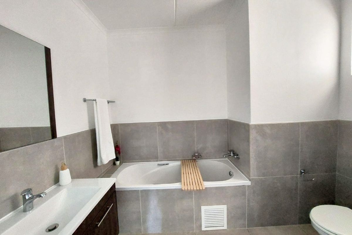 A modern, well-maintained bathroom featuring a built-in bathtub, vanity cabinet with basin, and neutral grey wall tiling.