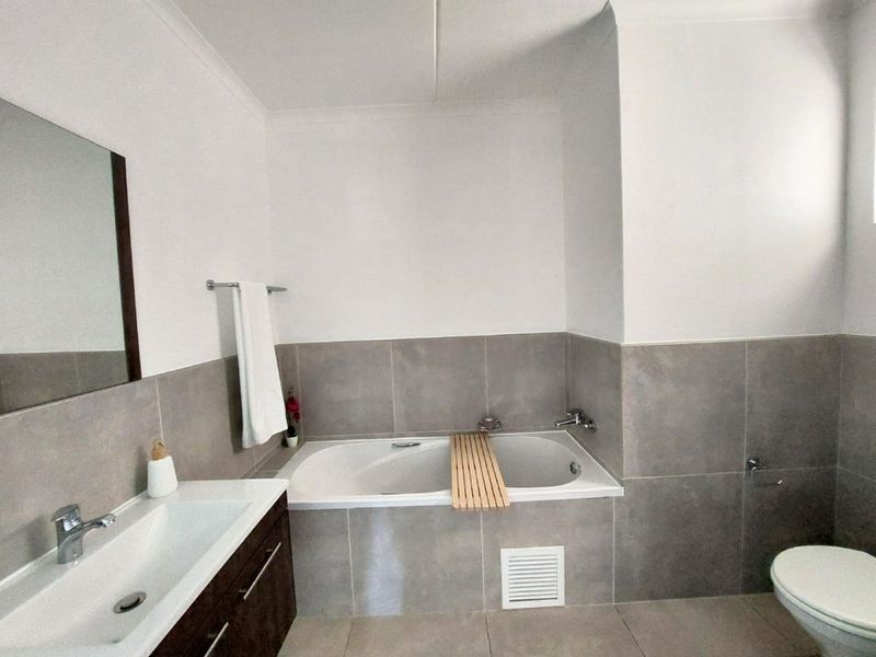 A modern, well-maintained bathroom featuring a built-in bathtub, vanity cabinet with basin, and neutral grey wall tiling.
