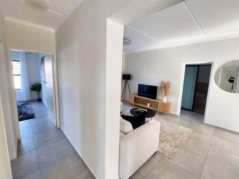 A bright, open-plan living area featuring neutral tiled flooring, clean white walls, and direct access to adjacent rooms through internal doorways.