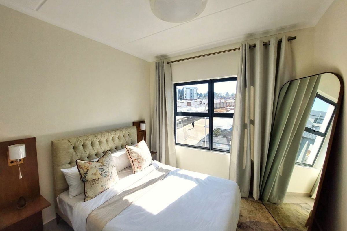 A well-lit bedroom featuring a built-in headboard with integrated bedside lighting and large aluminium-framed windows providing natural light.