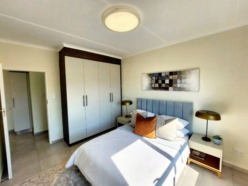 A well-maintained bedroom featuring neutral tiled flooring, a modern built-in wardrobe with dark frame detailing, and a central ceiling light fixture.
