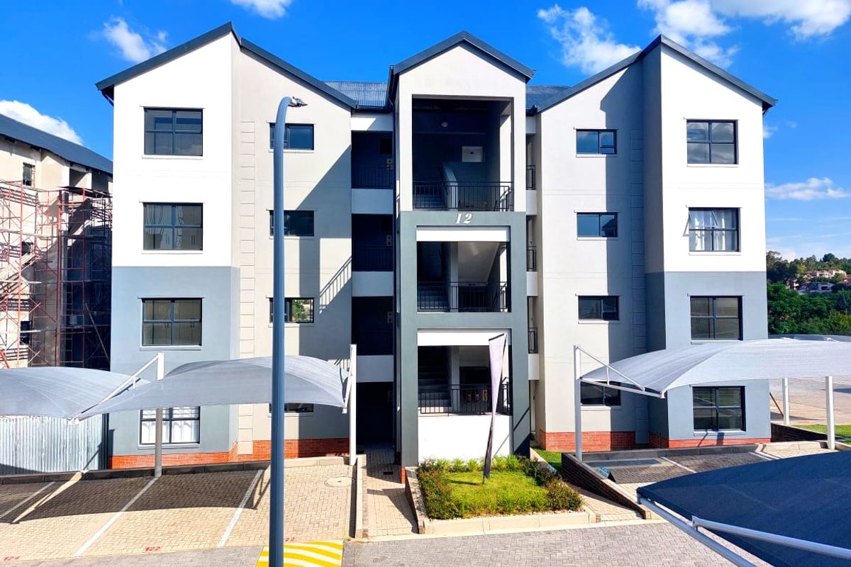 Front elevation of a modern multi-story apartment complex featuring paved parking areas with shade cloth carports and a central stairwell entrance.