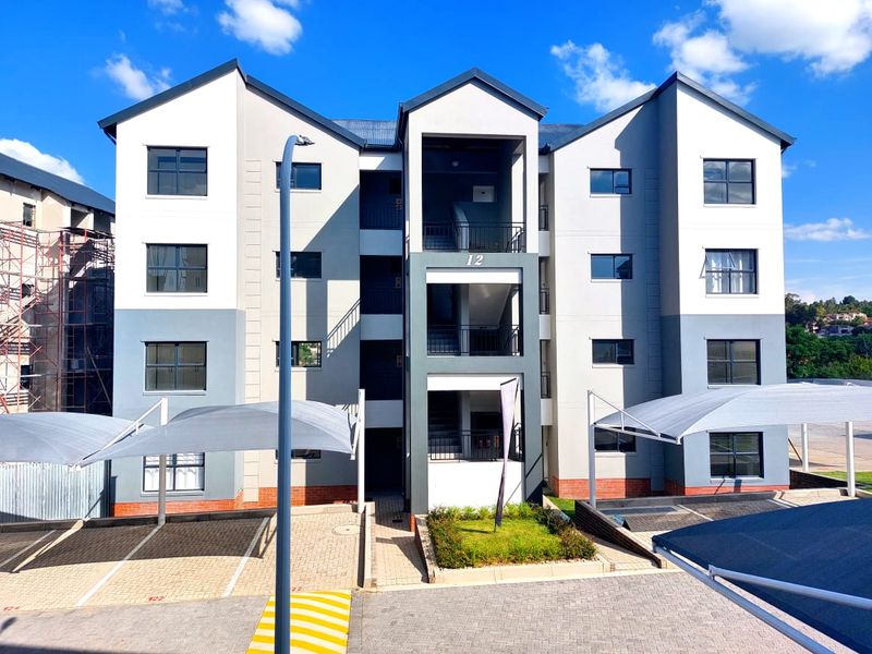Front elevation of a modern multi-story apartment complex featuring paved parking areas with shade cloth carports and a central stairwell entrance.