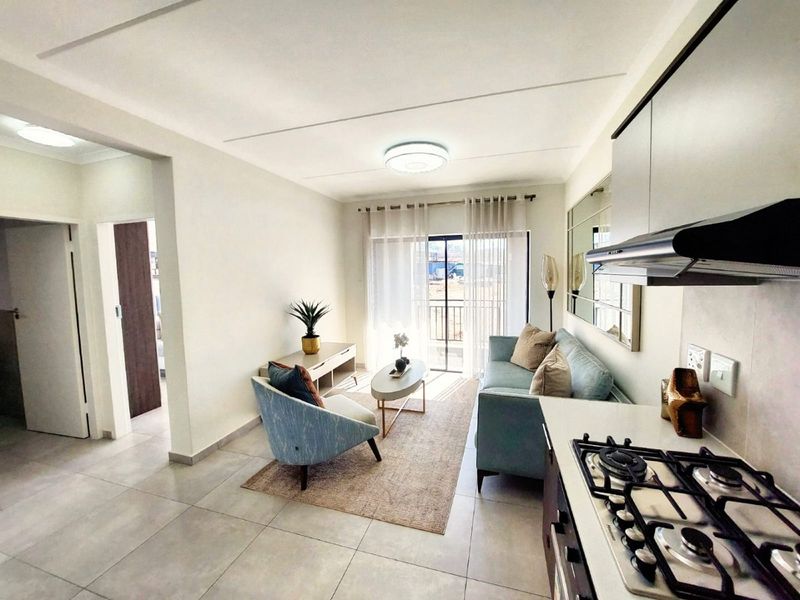 Modern open-plan living area featuring a functional kitchen with gas hob and extractor, flowing into a bright lounge with access to a balcony.