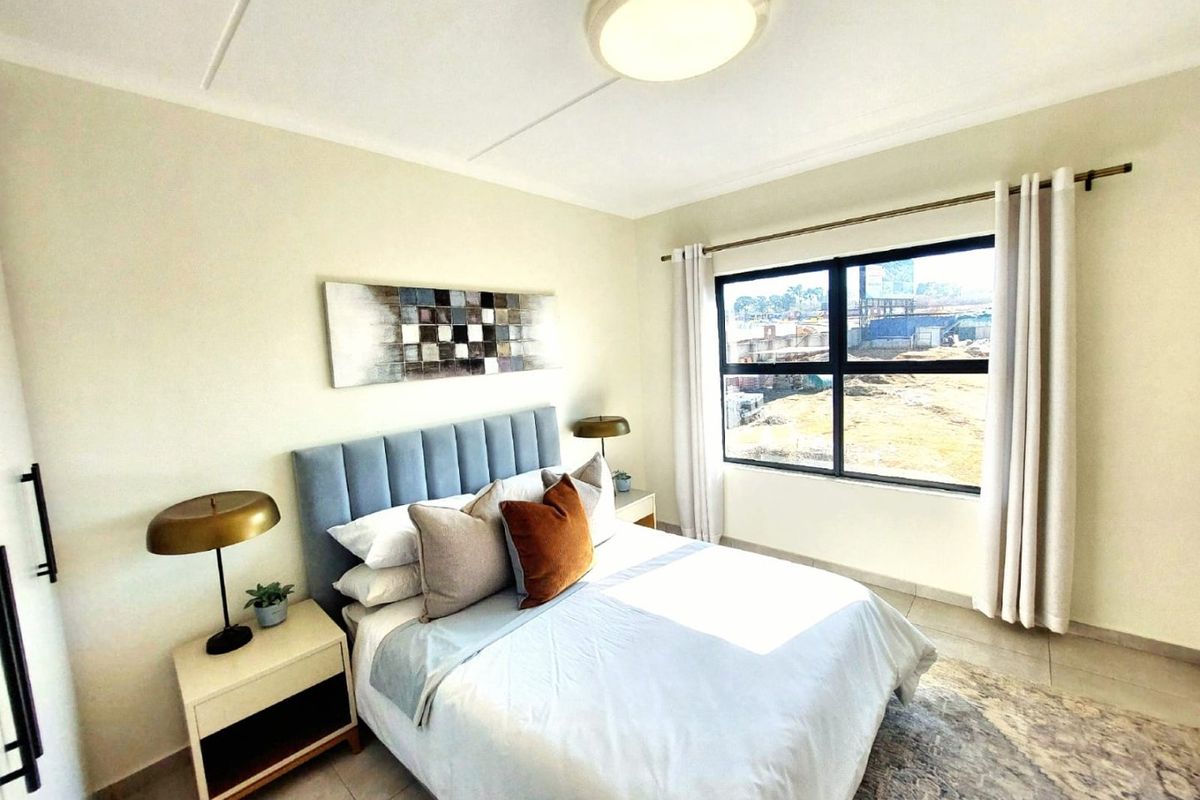 A well-lit bedroom featuring neutral walls, tiled flooring, and a large window providing natural light and exterior views.