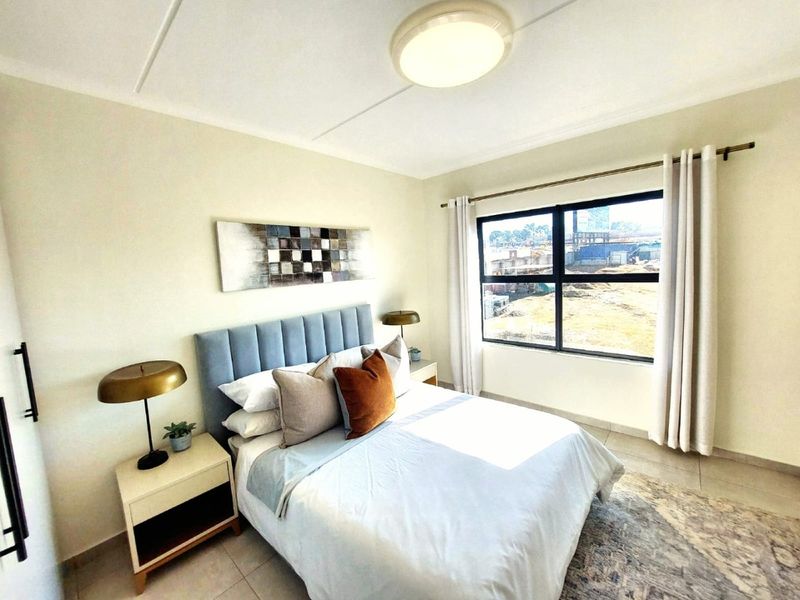 A well-lit bedroom featuring neutral walls, tiled flooring, and a large window providing natural light and exterior views.
