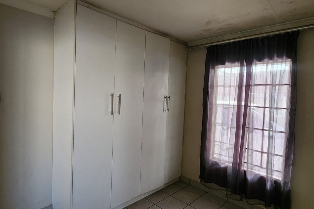 A bedroom featuring built-in cupboards, tiled flooring, and security bars on the window. The ceiling shows signs of water damage.