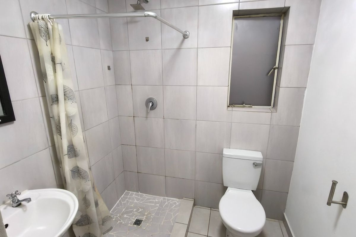 A functional bathroom featuring a shower with a mosaic tiled floor, a standard toilet, and a wall-mounted basin with neutral wall tiling.