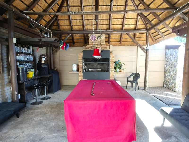 Covered outdoor entertainment area featuring a thatched roof, exposed timber beams, and a built-in braai, providing a rustic space for social gatherings.