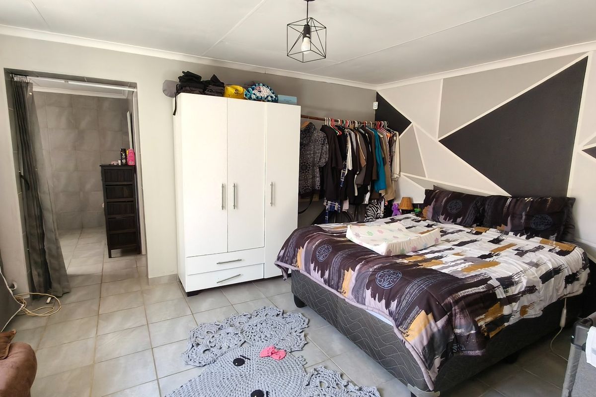 A bedroom featuring tiled flooring, a geometric accent wall, and an adjoining bathroom area.
