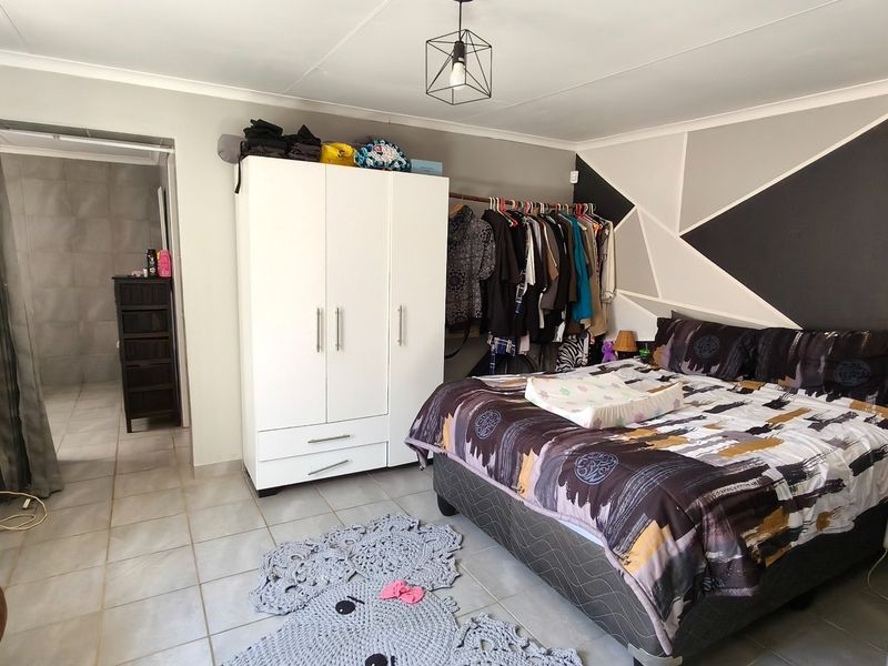 A bedroom featuring tiled flooring, a geometric accent wall, and an adjoining bathroom area.