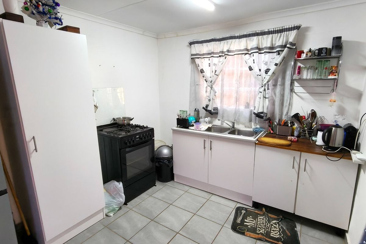 A functional kitchen featuring tiled flooring, built-in cabinetry, a stainless steel sink, and a freestanding stove, offering potential for modernization and aesthetic updates.