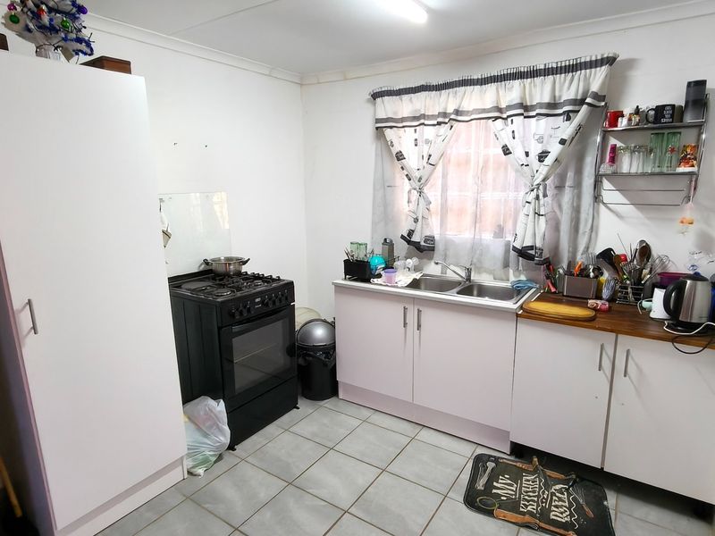 A functional kitchen featuring tiled flooring, built-in cabinetry, a stainless steel sink, and a freestanding stove, offering potential for modernization and aesthetic updates.