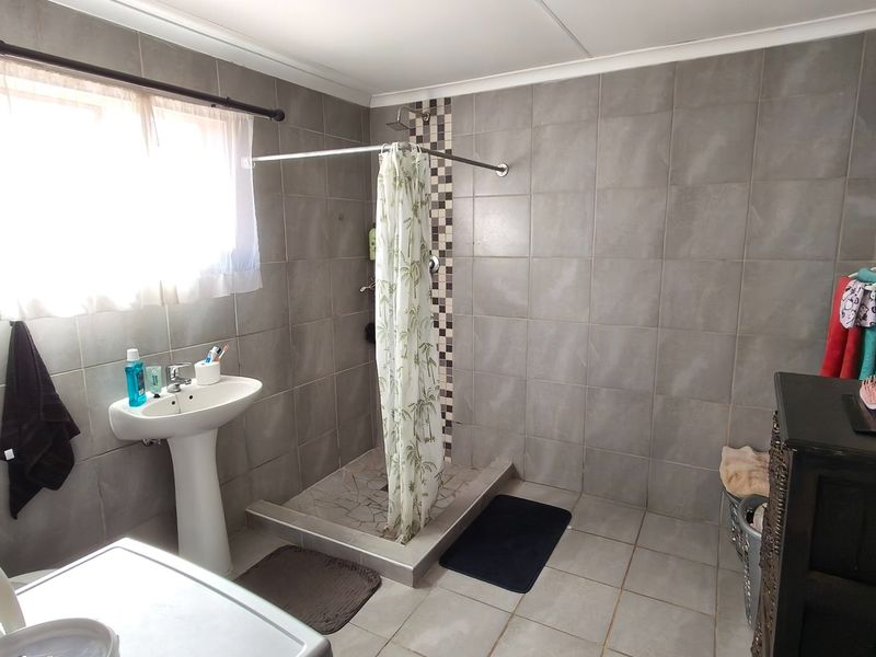 A functional bathroom featuring a walk-in shower with tiled surround and a pedestal basin, finished with neutral wall and floor tiles.