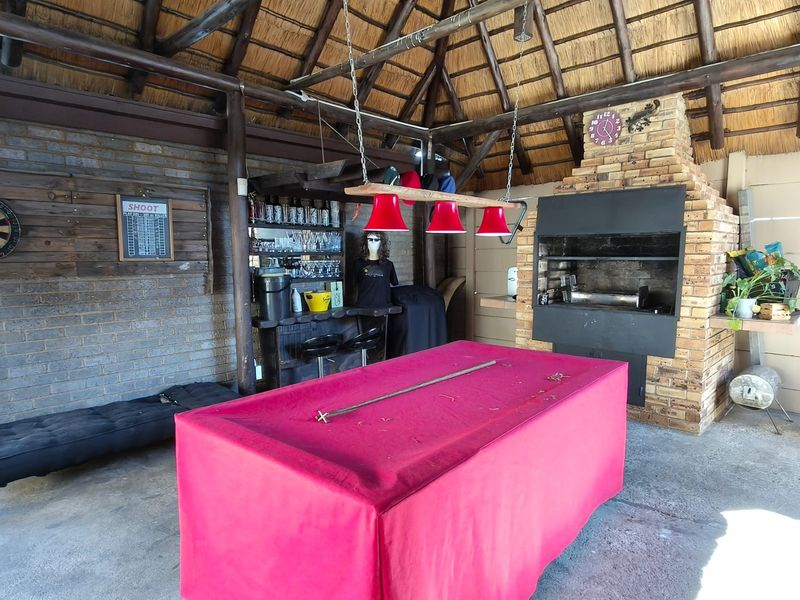 Covered outdoor entertainment area featuring a thatched roof, exposed timber beams, and a built-in brick braai, ideal for social gatherings.
