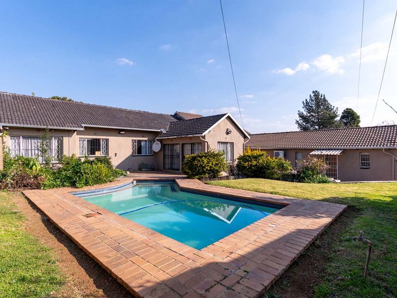 Rear exterior view featuring a swimming pool with brick coping, set within a landscaped garden and adjacent to the main dwelling and outbuilding.