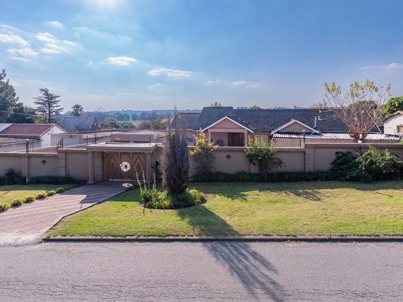 Front view of the property featuring a paved driveway, secure perimeter wall with electric fencing, and a gated entrance.