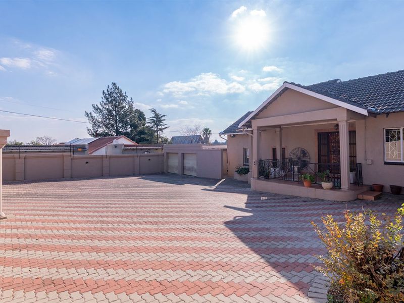 Spacious front exterior featuring a large paved driveway, covered entrance porch, and secure perimeter walling with integrated garage access.