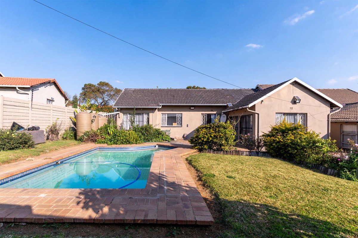 Rear view of the property featuring a swimming pool with brick surround, landscaped garden, and water storage tanks against a precast boundary wall.