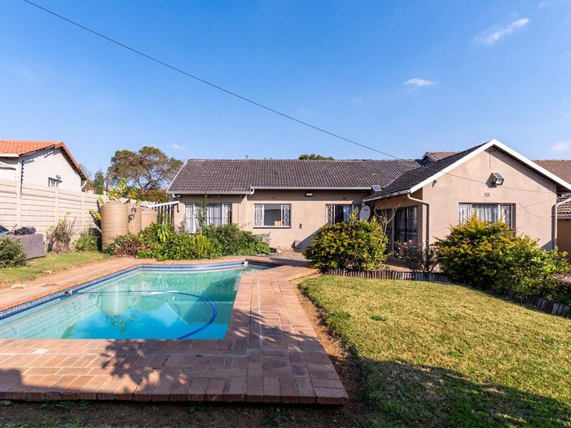 Rear view of the property featuring a swimming pool with brick surround, landscaped garden, and water storage tanks against a precast boundary wall.