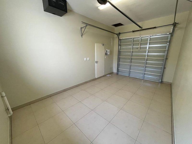 A clean, empty garage featuring tiled flooring, a sectional garage door, and internal access door, providing secure parking and storage space.
