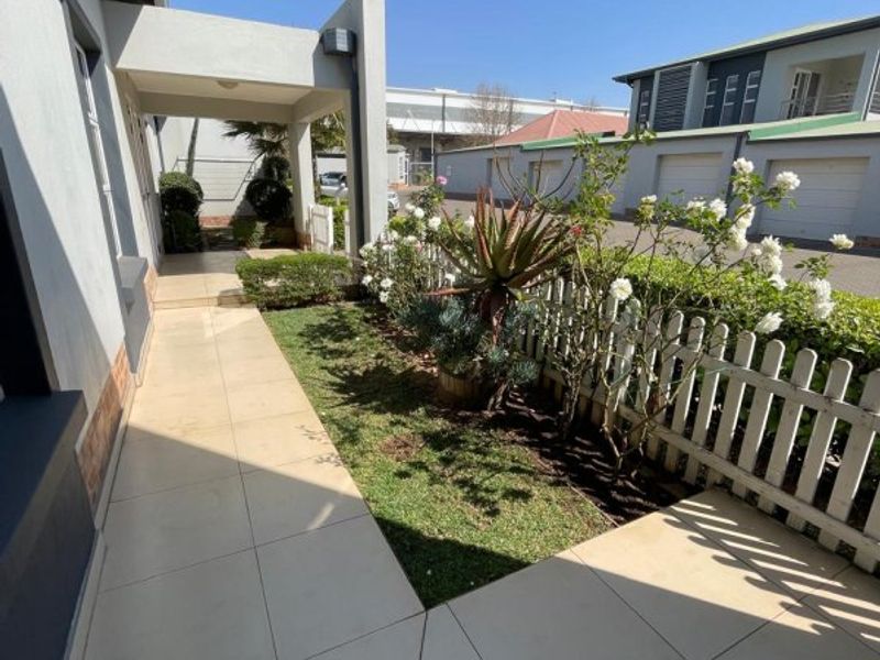 A well-maintained front entrance area featuring a tiled walkway, covered porch, and a neat garden bed enclosed by a white picket fence.