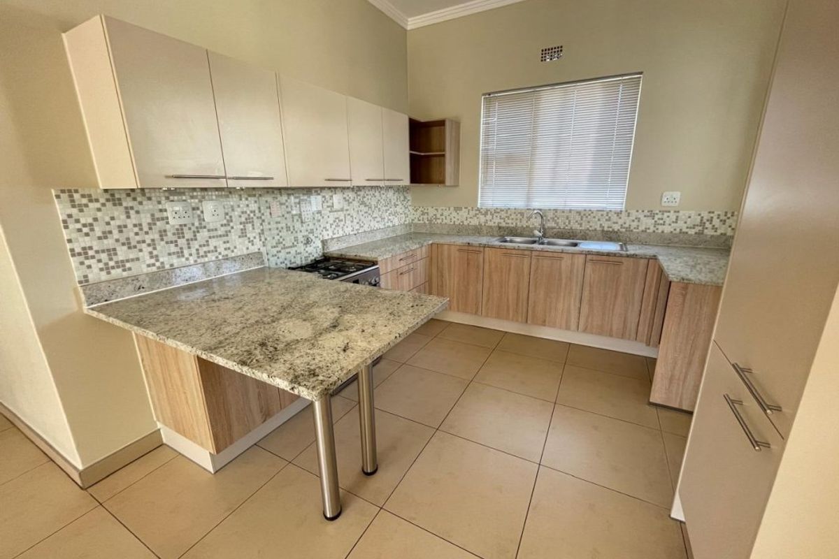 A clean, functional kitchen featuring granite countertops, mosaic tile backsplash, ample laminate cabinetry, and a built-in gas hob with a breakfast nook.