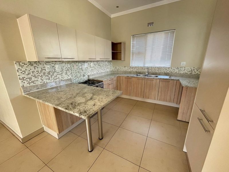 A clean, functional kitchen featuring granite countertops, mosaic tile backsplash, ample laminate cabinetry, and a built-in gas hob with a breakfast nook.