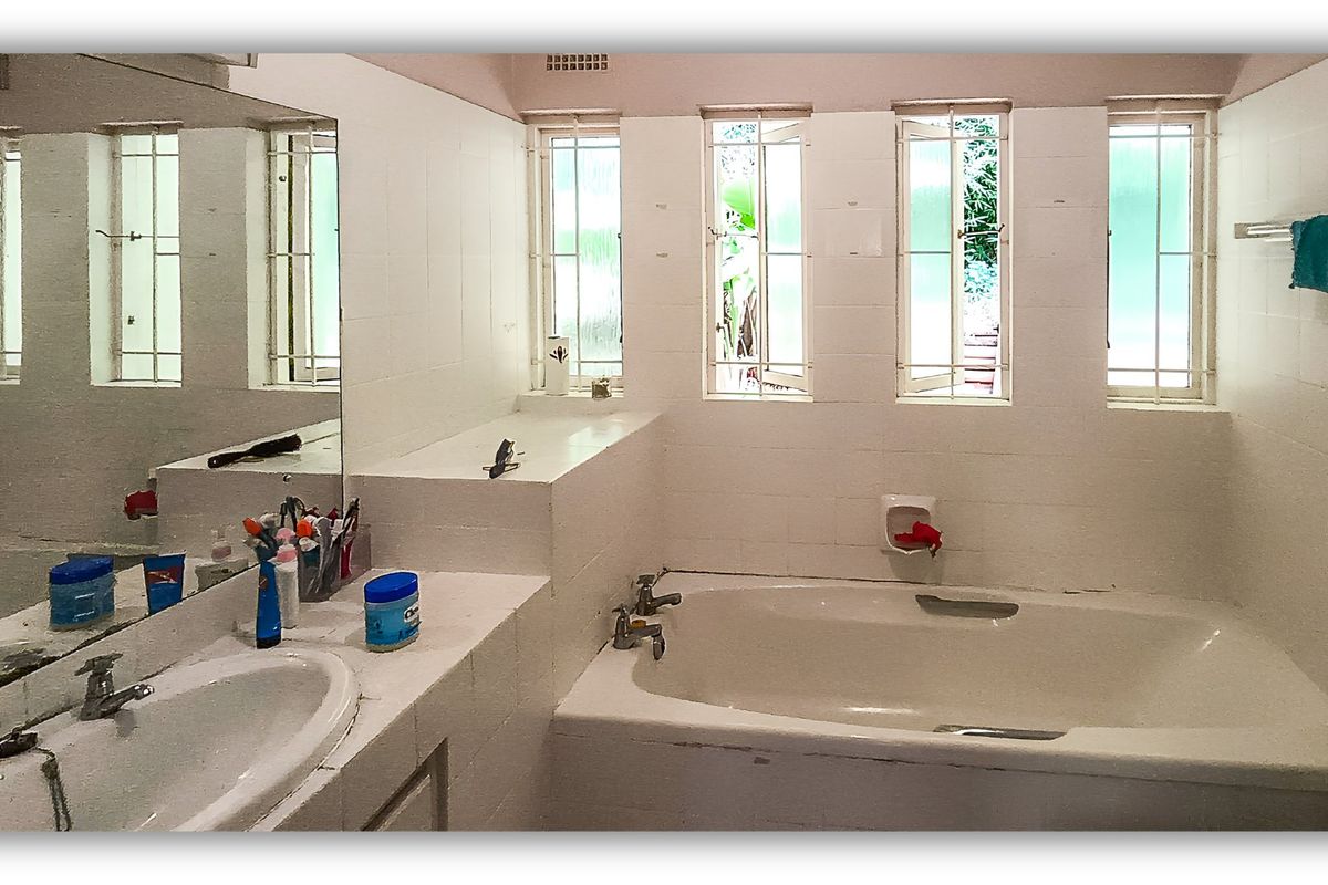 A dated bathroom featuring a built-in bathtub, vanity basin, and multiple windows with security bars, offering a functional layout ready for modernization.